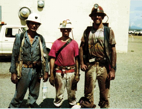 Photo of three guys in
          mining clothes standing in the hot Arizona sun. They are
          wearing hard hats with lamps and have heavy mining gear belts
          on. They have just returned from to the surface after working
          underground all day. They are comopletely covered with dark
          blasted rock dust. Their names are Marco Einaudi, Guillermo
          Pareja, and Kurt Friehauf.