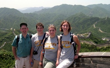Dr. Kurt Friehauf with three Kutztown University students
          sitting high on the Great Wall of China. The wall continues
          into the distance, snaking along the ridges of rugged green
          mountains.
