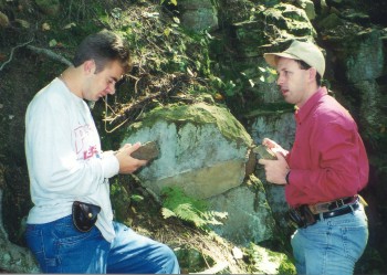 Dr. Kurt Friehauf with a student examining
            moss-covered iron ores of the Mid-Atlantic iron belt. Dr.
            Friehuaf has a belt armed with a large geologic hammer and a
            geologic compass. The photo caught him in mid-sentence, so
            his mouth is open, making him look a little dorky.